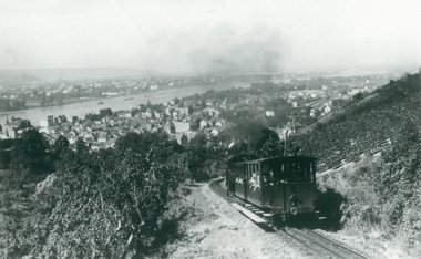 Steam locomotive with 2 demonstration cars travelling uphill, in the background the Rhine and Königswinter.